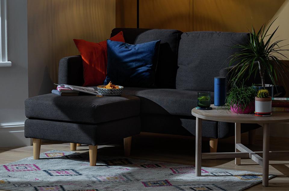 The charcoal Habitat Remi 2-seater fabric chaise in a box sofa in a dark but cosy lounge setting.