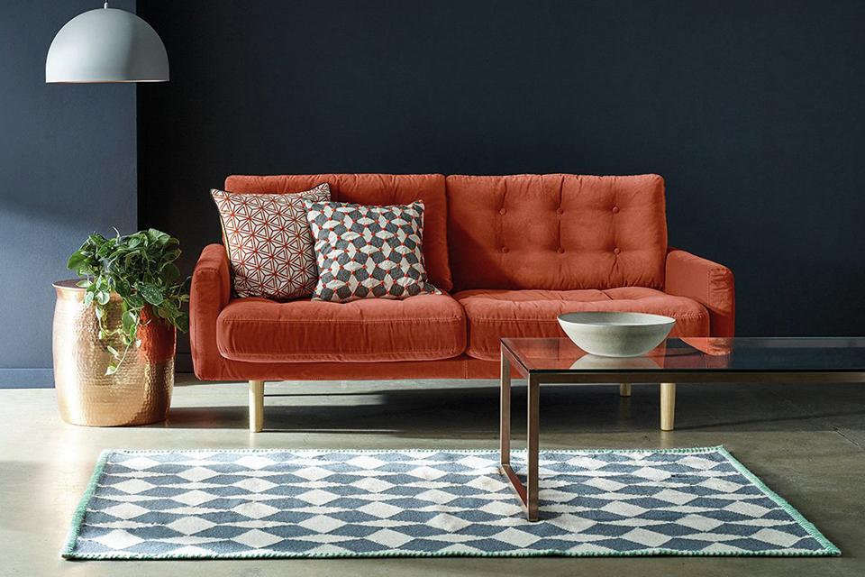 The orange Habitat Fenner velvet sofa in a navy lounge setting.