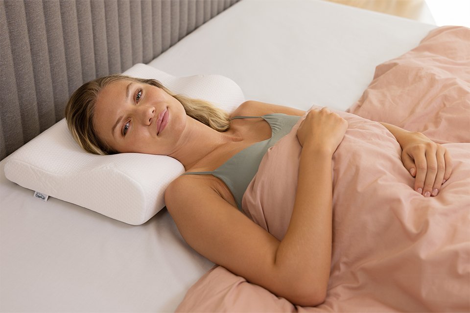 A woman resting her head and neck on a TEMPUR® ergonomic pillow. 