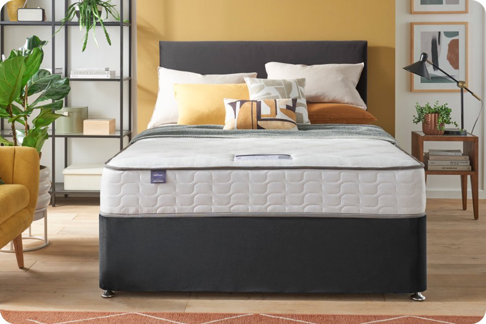 A bed arranged with Silentnight mattress, pillows, cushions and a blanket.