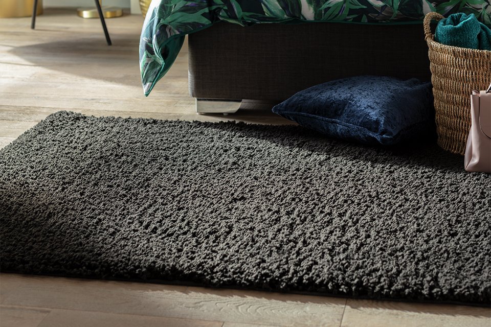 A Habitat cosy black shaggy rug placed in front of a bed.