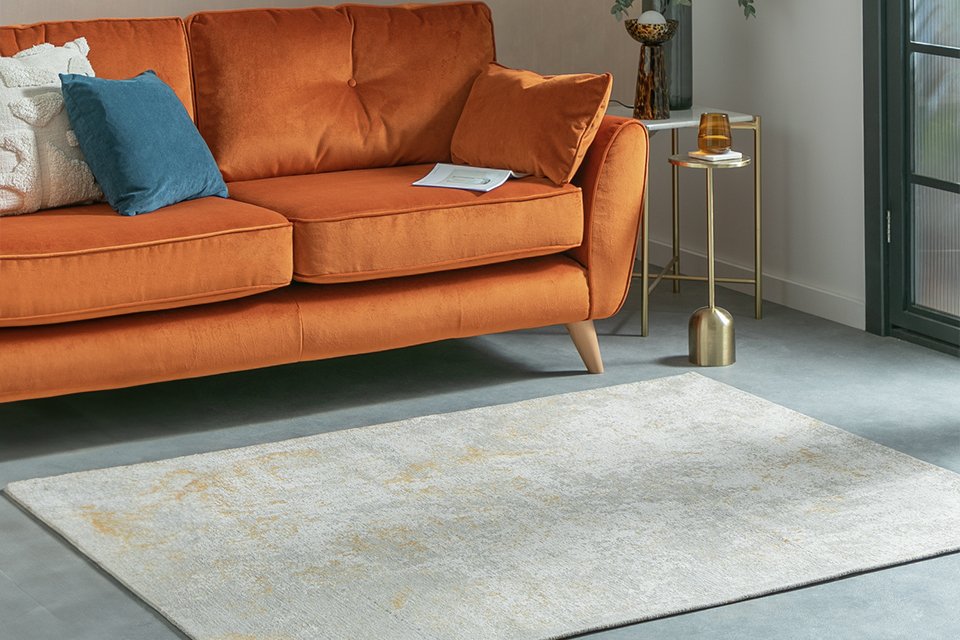 A Habitat distressed abstract gold flatweave rug placed in front of a sofa in a living room.