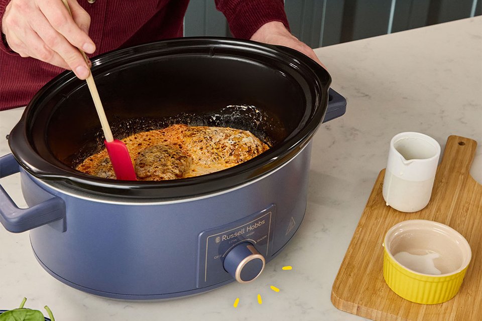 A person cooking a meal in a Russell Hobbs 7L slow cooker.