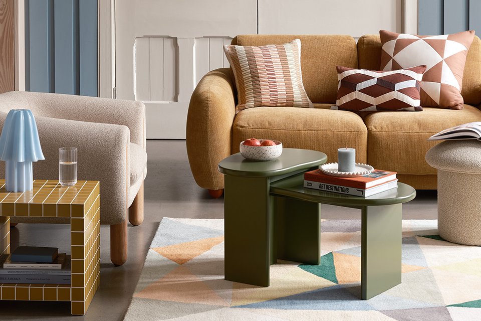 A living room designed with a collection of Habitat products including a green nested coffee table, boucle armchair, brown sofa, and a mustard yellow side table and more.