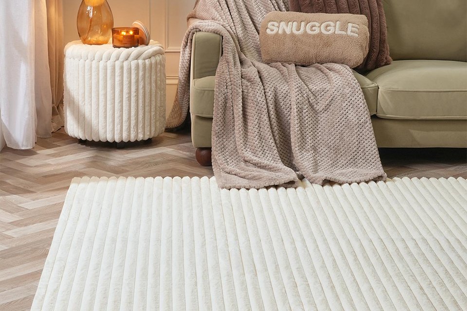 An OHS faux fur ribbed fleece rug placed next to a sofa and a side table in a living room.