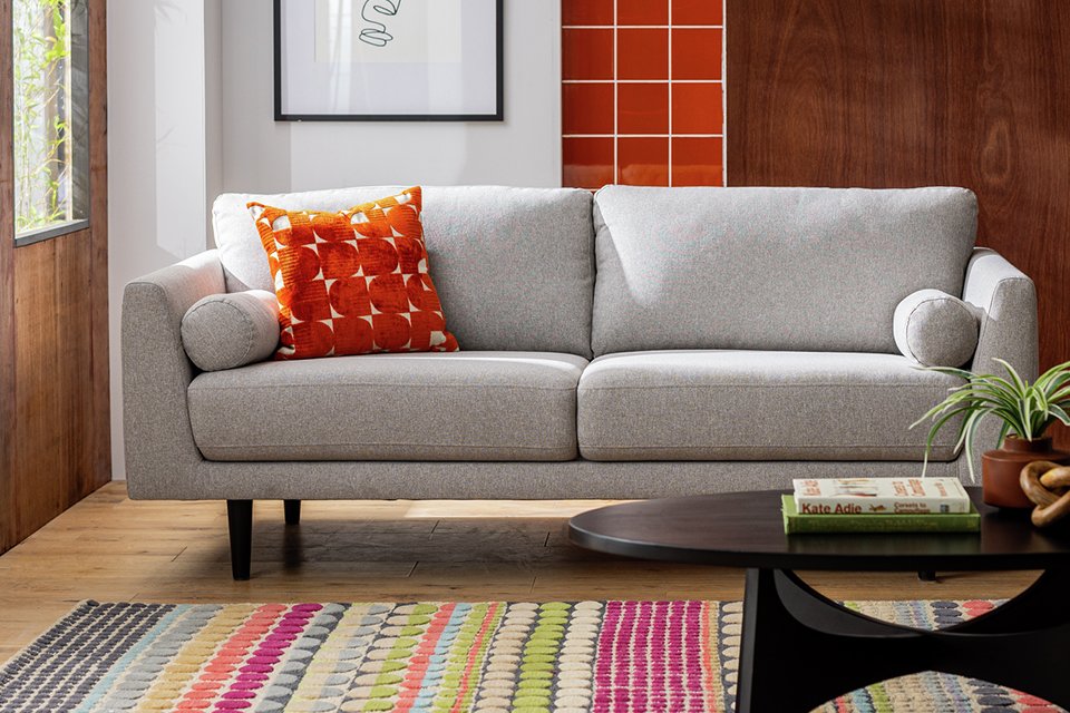 An orange cushion on a grey sofa in a living room.