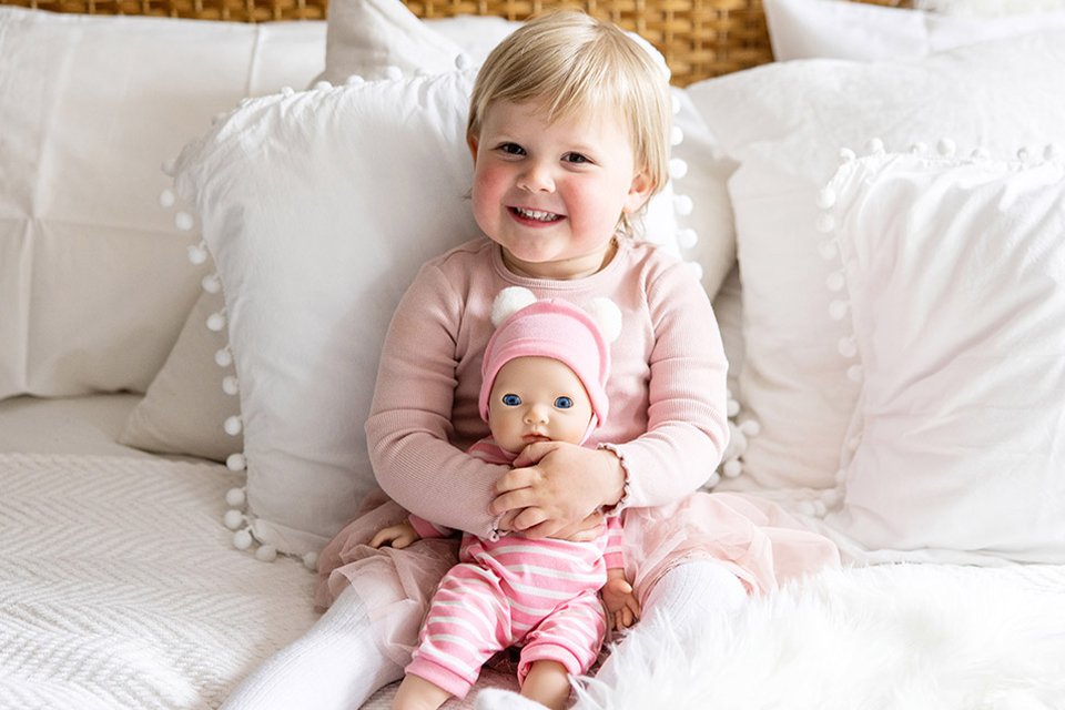 Toddler cuddling 36cm My First Tiny Treasures baby doll on bed. 