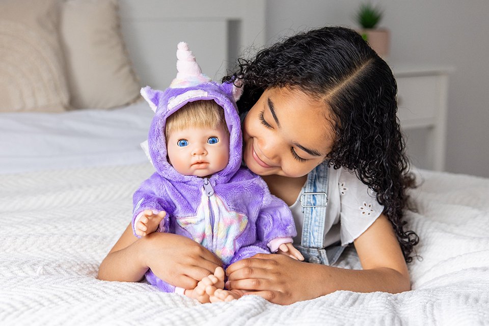 Girl cuddling 44cm Tiny Treasures baby doll dressed in Unicorn Star All In One outfit. 