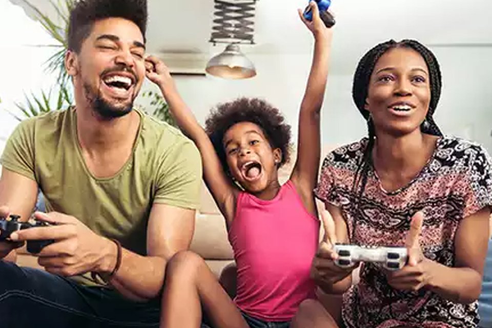 A family of 3 playing video game together on a sofa.