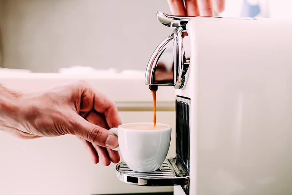 A mug is held under a coffee machine as it brews a fresh drink.