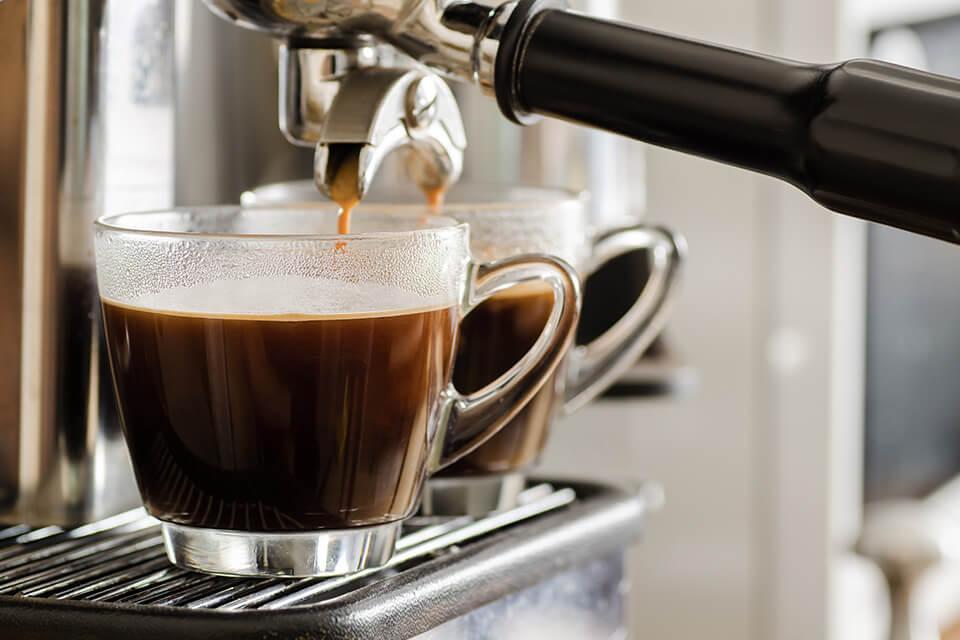 A coffee machine brews a fresh drink into a clear glass.