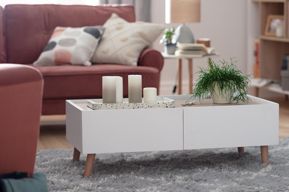 White, rectangular coffee table with wooden peg legs in front of a pink sofa.