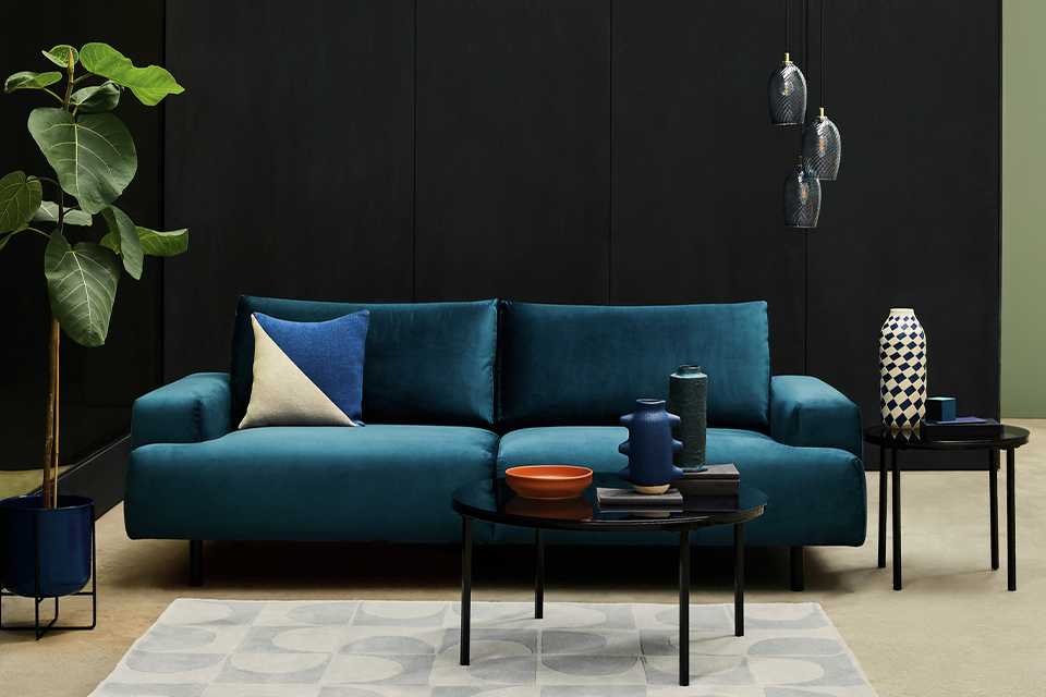 Black coffee table in front of a blue, velvet sofa.