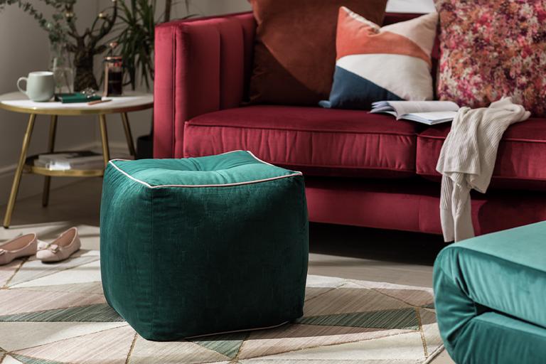 A velvet green pouffe in front of a sofa in a living room.