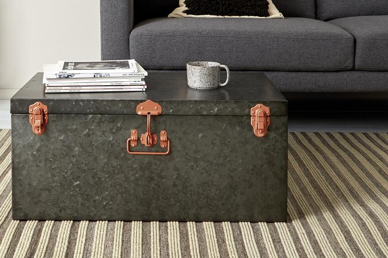 A large metal trunk placed in place of a coffee table in a living room.