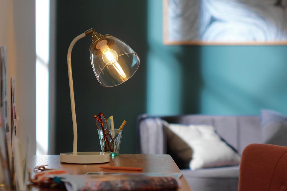 An cream coloured desk lamp with a glass shade on a table in a green room.