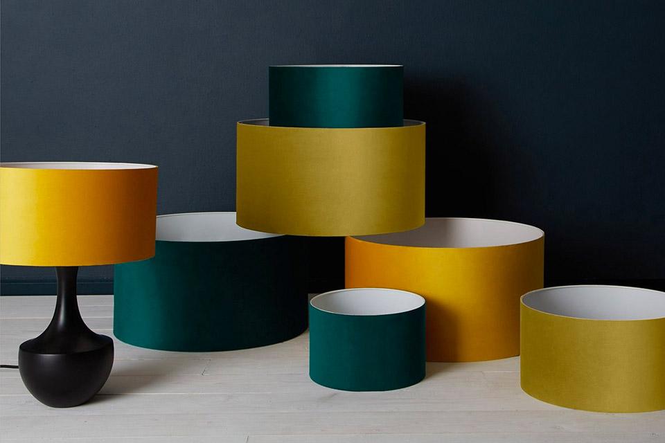 Collection of velvet drum lamp shades in green and yellow displayed in front of a black background.