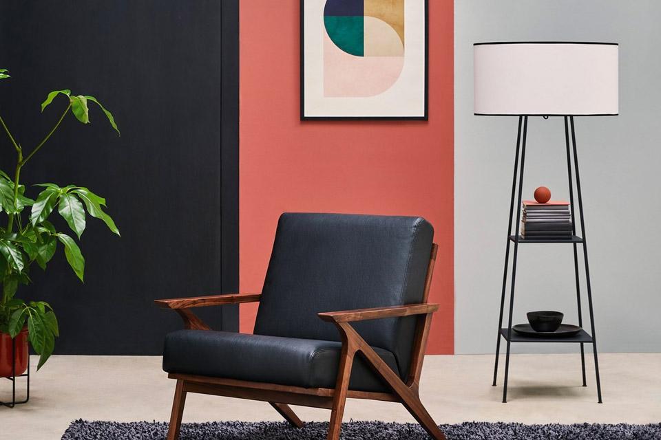 Image of a lamp with shelves next to black armchair.