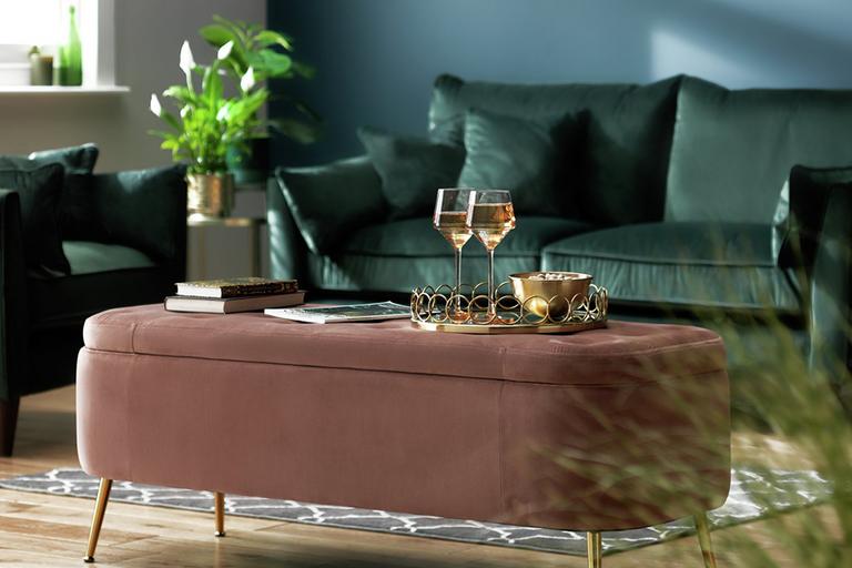 A pink ottoman used as a coffee table in a living room.