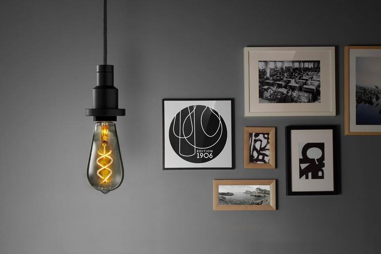 Image of exposed filament bulb against a backdrop of framed pictures.