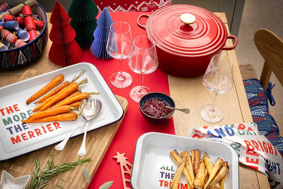 Roasted veggies in different festive trays and a red pot with lid on a table.