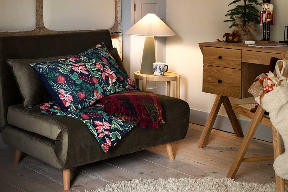 A leaf-printed cushion and a throw on a sofa bed in a bedroom.