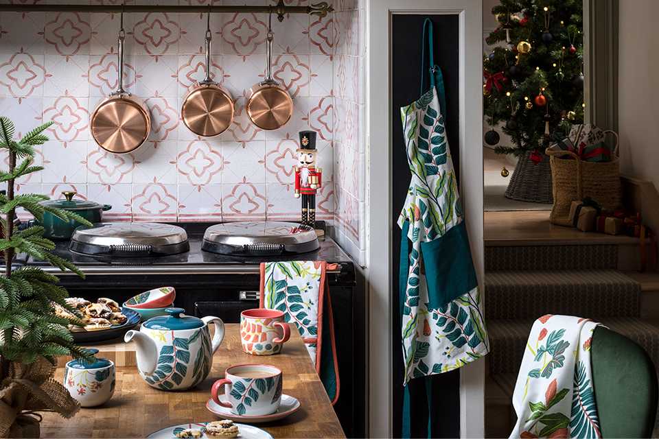 A kitchen set up with different pots hanging against the wall and kitchen towel and oven mitts on the chair.