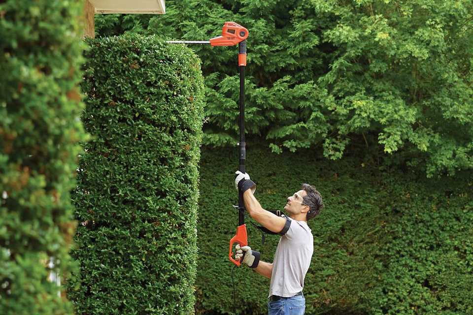 A man trimming the bushes with a Black Decker hedge trimmer.