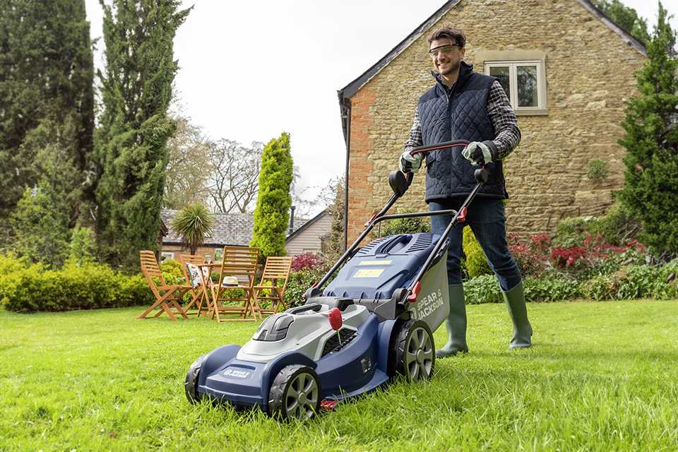 A man using a Spear and Jackson cordless rotary lawnmower.