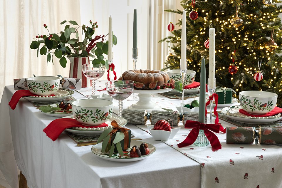 Candles, red ribbons, and little presents used to decorate a Christmas dinner table.