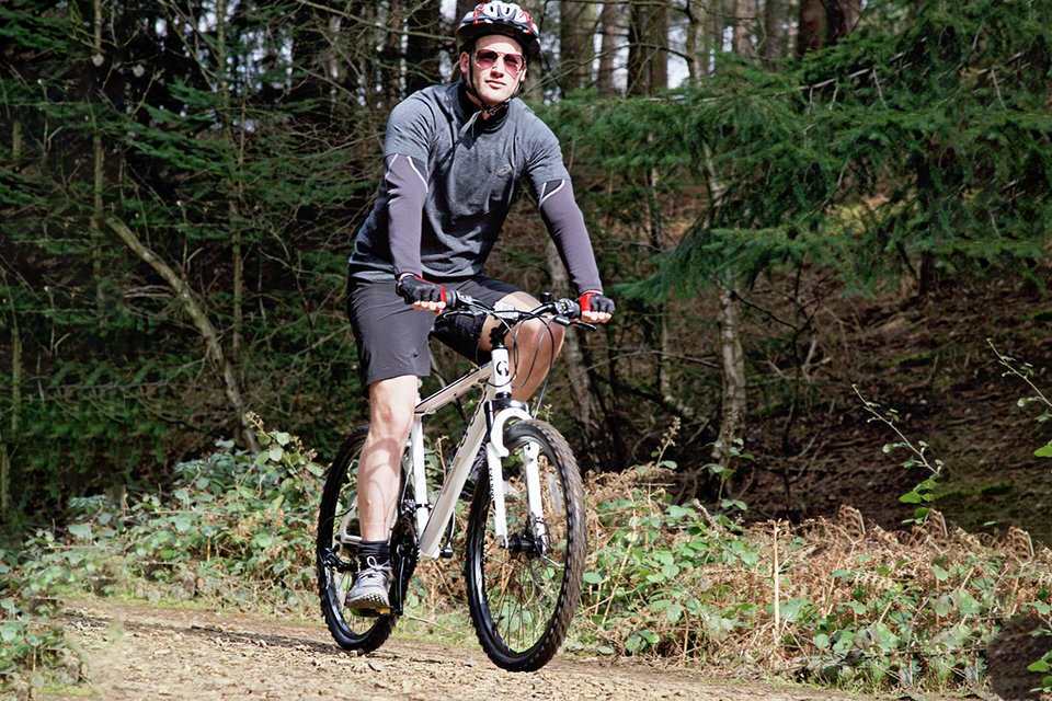 A man riding Cross FXT30 26 inch Wheel Size Mens Mountain Bike.