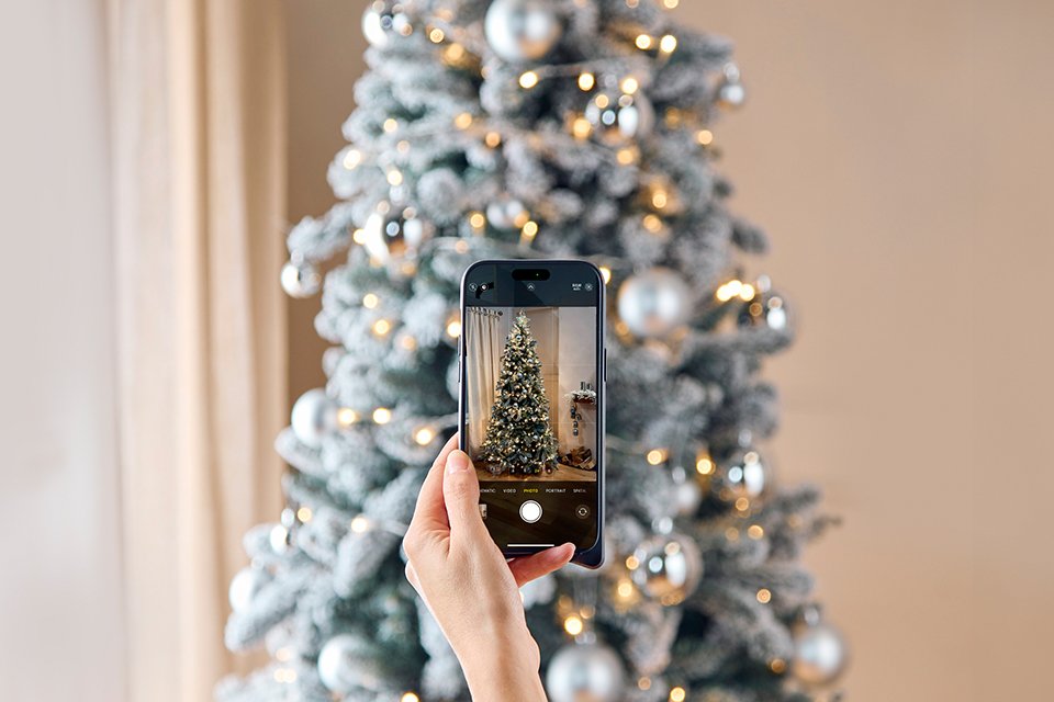 A person viewing a Christmas tree in their home through a mobile phone.