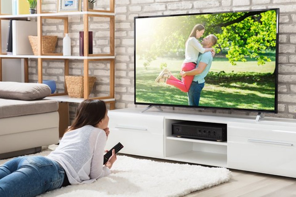 A woman is watching a movie on the TV while lying on a carpet in a living room setup. 