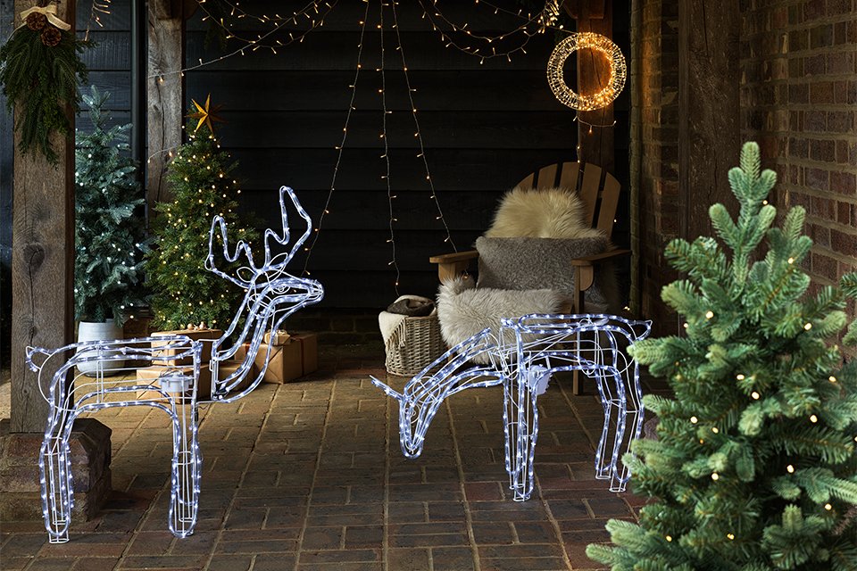 A decorated porch of a house with Habitat outdoor Christmas lighting, two reindeer figurines, and a tree.