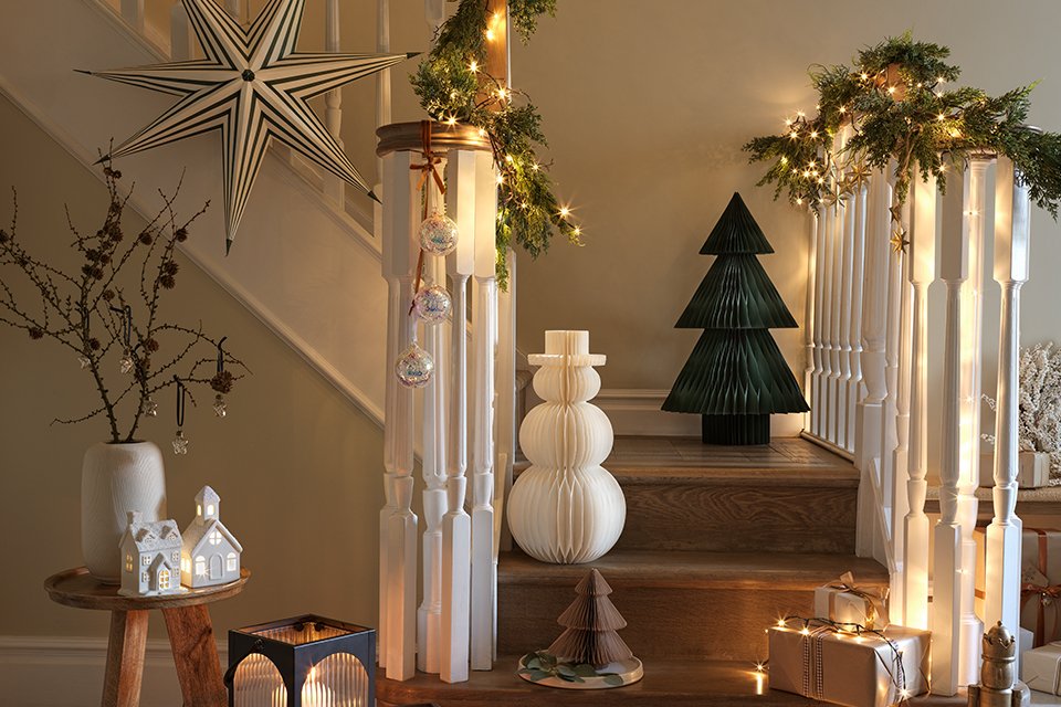 An indoor staircase decorated with a star, a small tree and a snowman figure, lamps and lights.