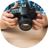 A person configuring a DSLR camera with two other cameras placed on the table.