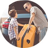A father and son putting a yellow coloured suitcase in the car boot.