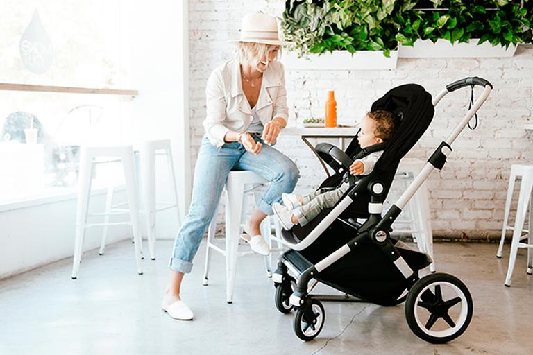 Mother sitting with her baby next to her in a black Bugaboo pushchair.