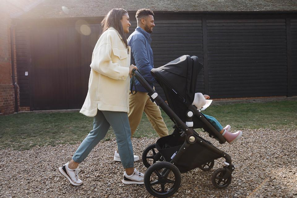 Parents walking their baby in a black Bugaboo pushchair.