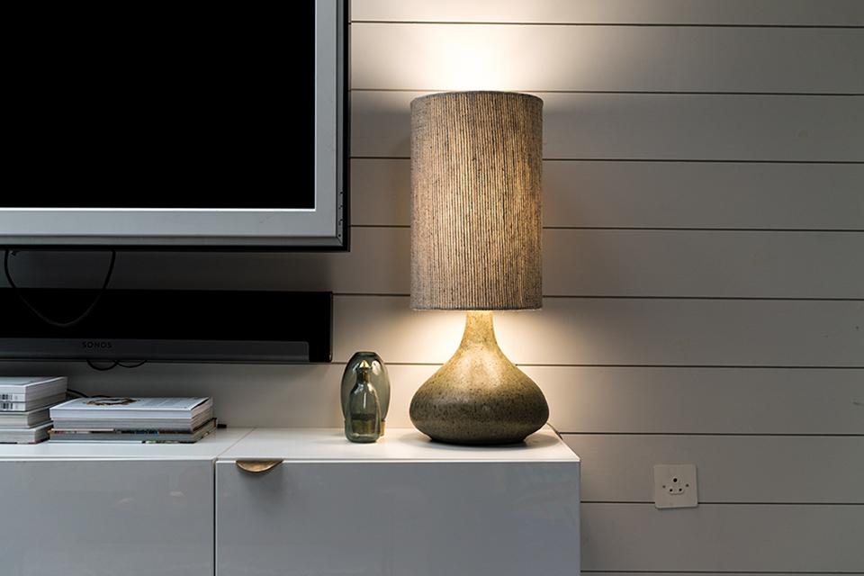 Image shows a wood-effect lampshade against a white wooden wall, emitting a warm gentle light.
