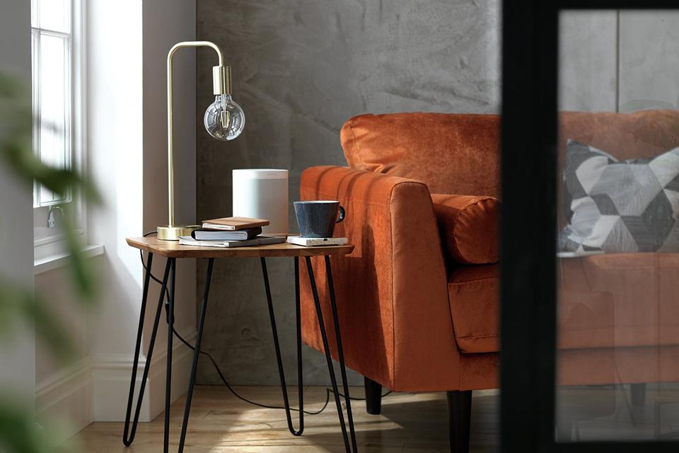 Image of round, brown side table with black hair pin legs next to a tan leather sofa.