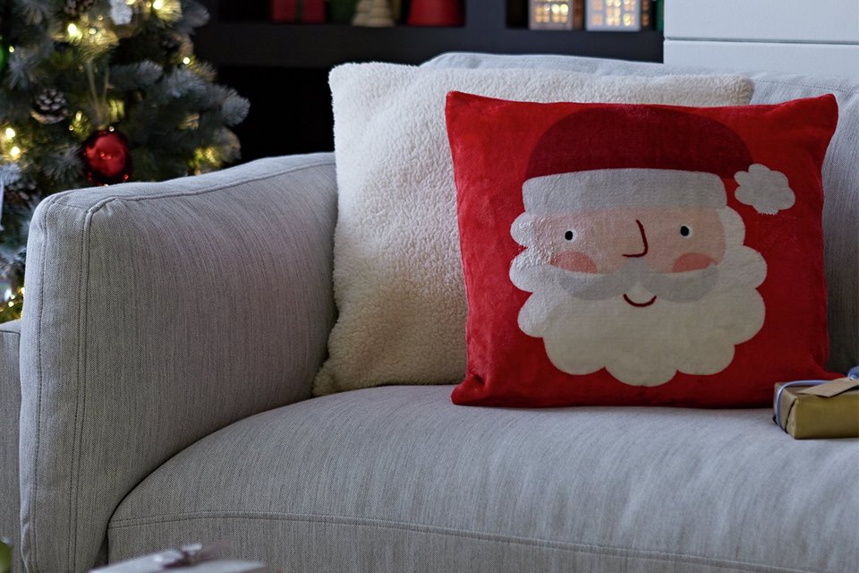 Argos Home Christmas Santa Printed Fleece Cushion in red and white colour placed on grey sofa.
