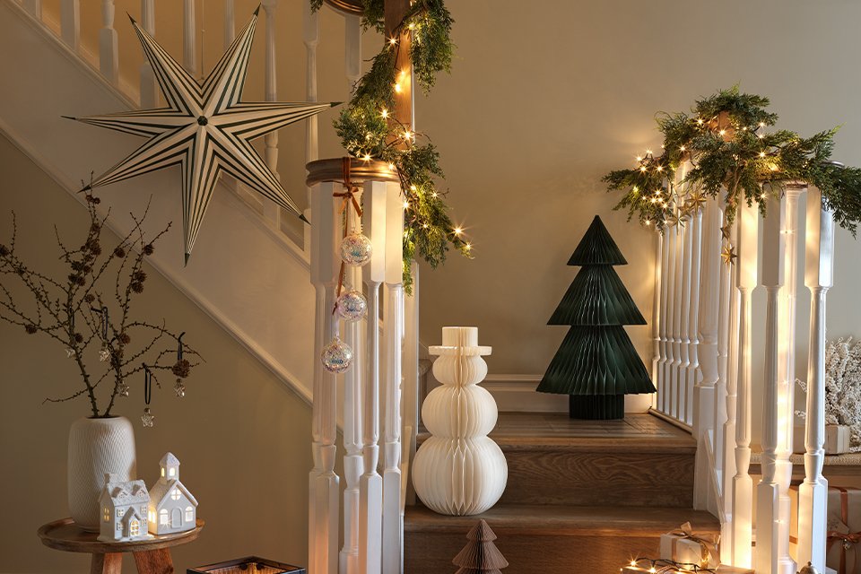 Christmas decorating items placed around a staircase on a display including lamps, lights, garlands, gift boxes etc.