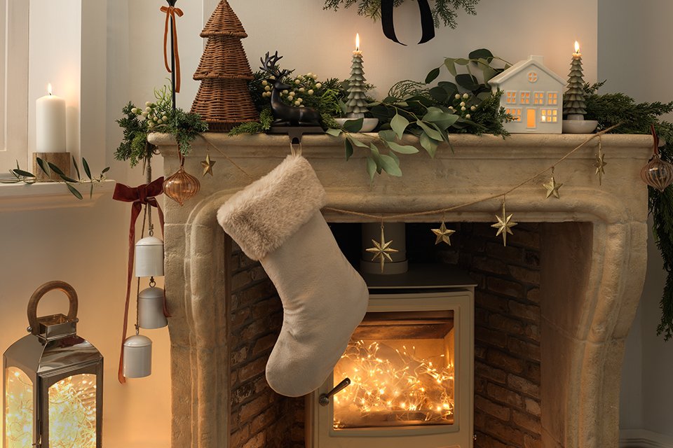 A mantel decorated for Christmas with a stocking, Christmas lights, garland, and other decoratives.