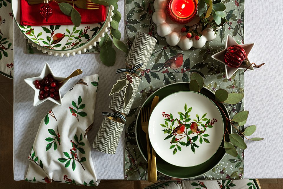 A table set with Habitat Red Robin red and green plates, bowls, and candles.