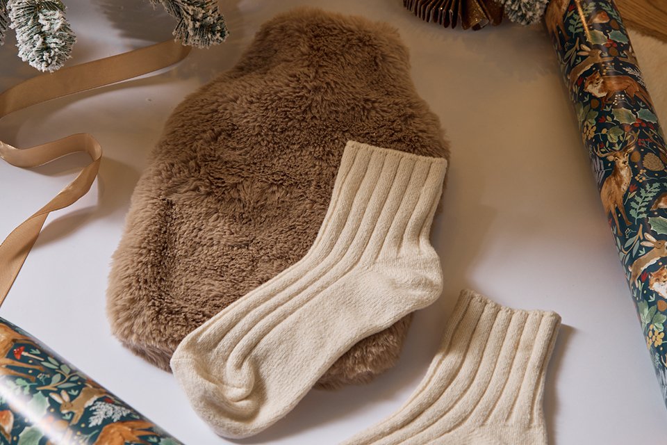 Brown faux fur water bottle and socks gift set situated on wrapping paper ready to be wrapped as a gift.