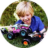 A little boy playing with Hot Wheels monster trucks in the garden.