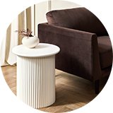 White ribbed side table next to brown velvet chair in living room .