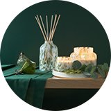 A collection of Habitat Christmas candles and reed diffuser placed on a wooden table with green background.