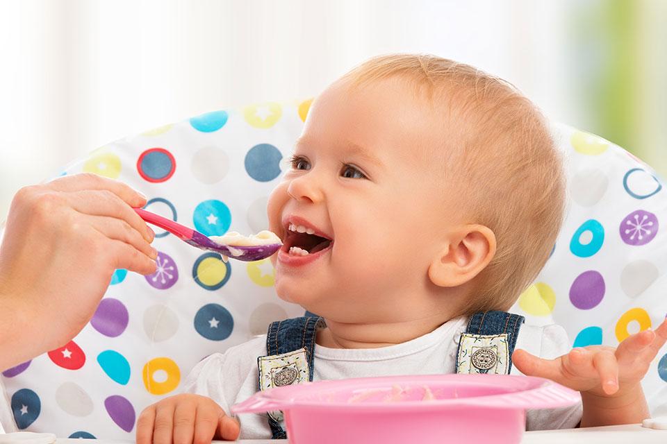 A smiling baby being fed on a highchair.